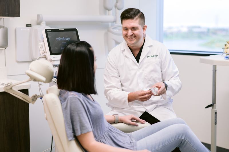 Dr. Bednar smiling and holding a model of the jaw while talking with a patient seated in an exam chair